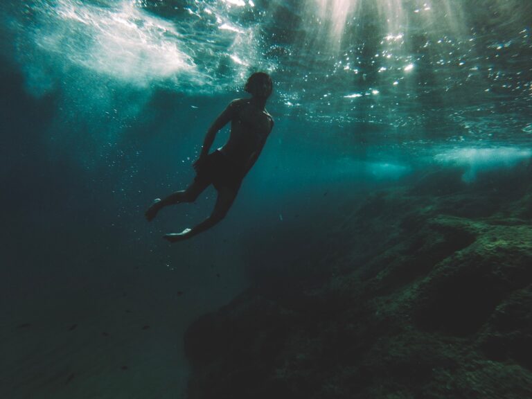 Silhouette of a diver exploring deep underwater surrounded by sunlight rays.